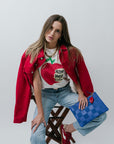 Woman wearing a red jacket and blue jeans, holding a blue handbag with a red heart, on a white background.