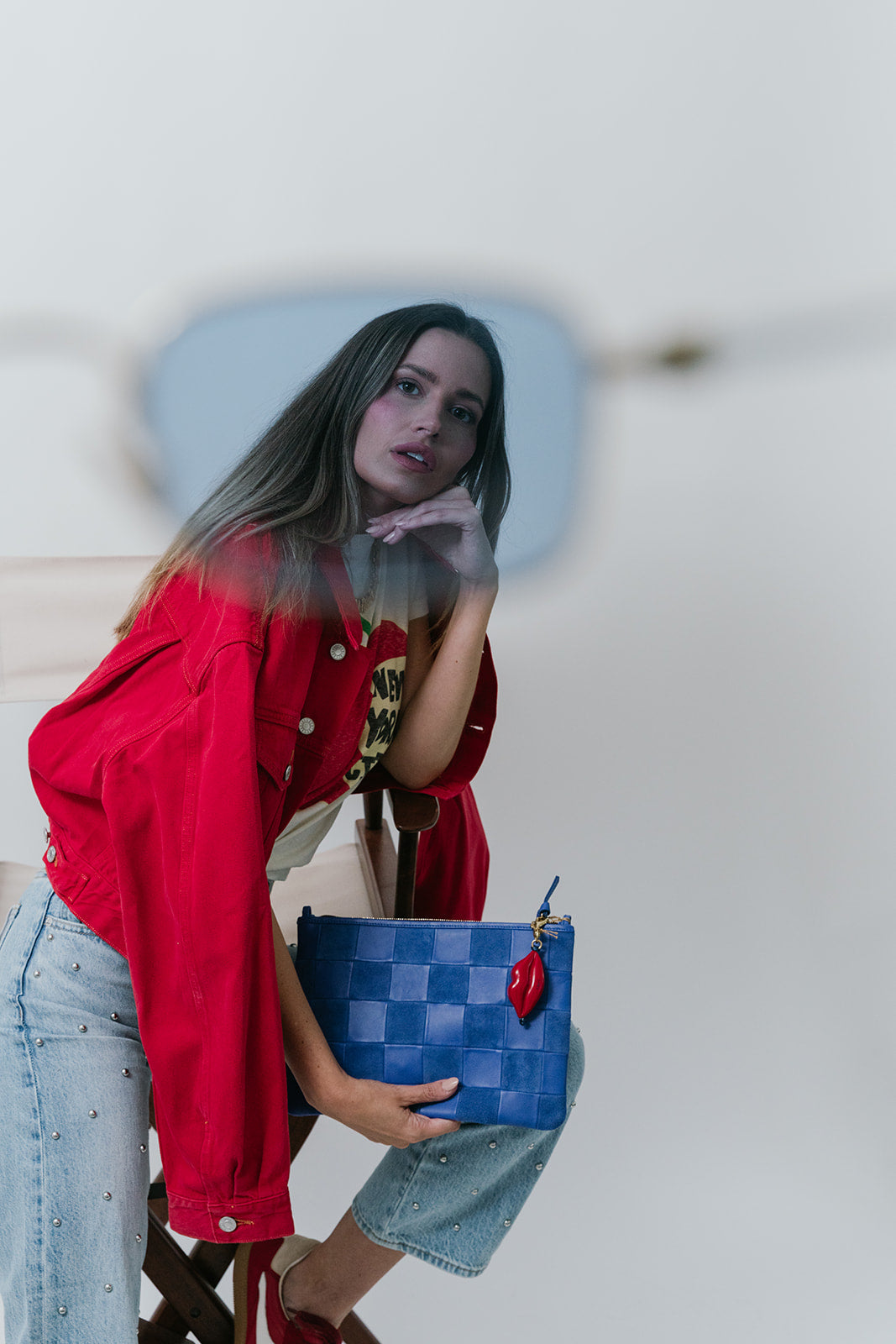 Woman holding a blue checkered bag with red lips fob against a white background