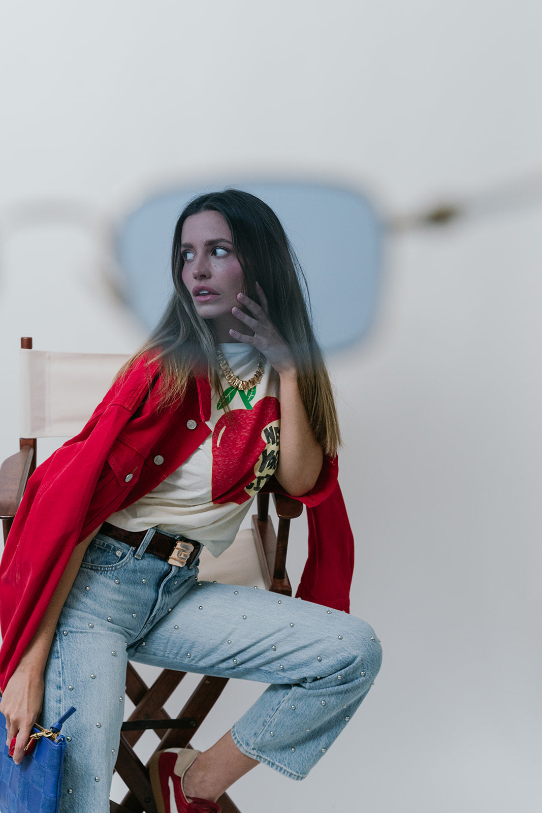 Woman in a red jacket and light blue jeans sitting on a chair with a white background