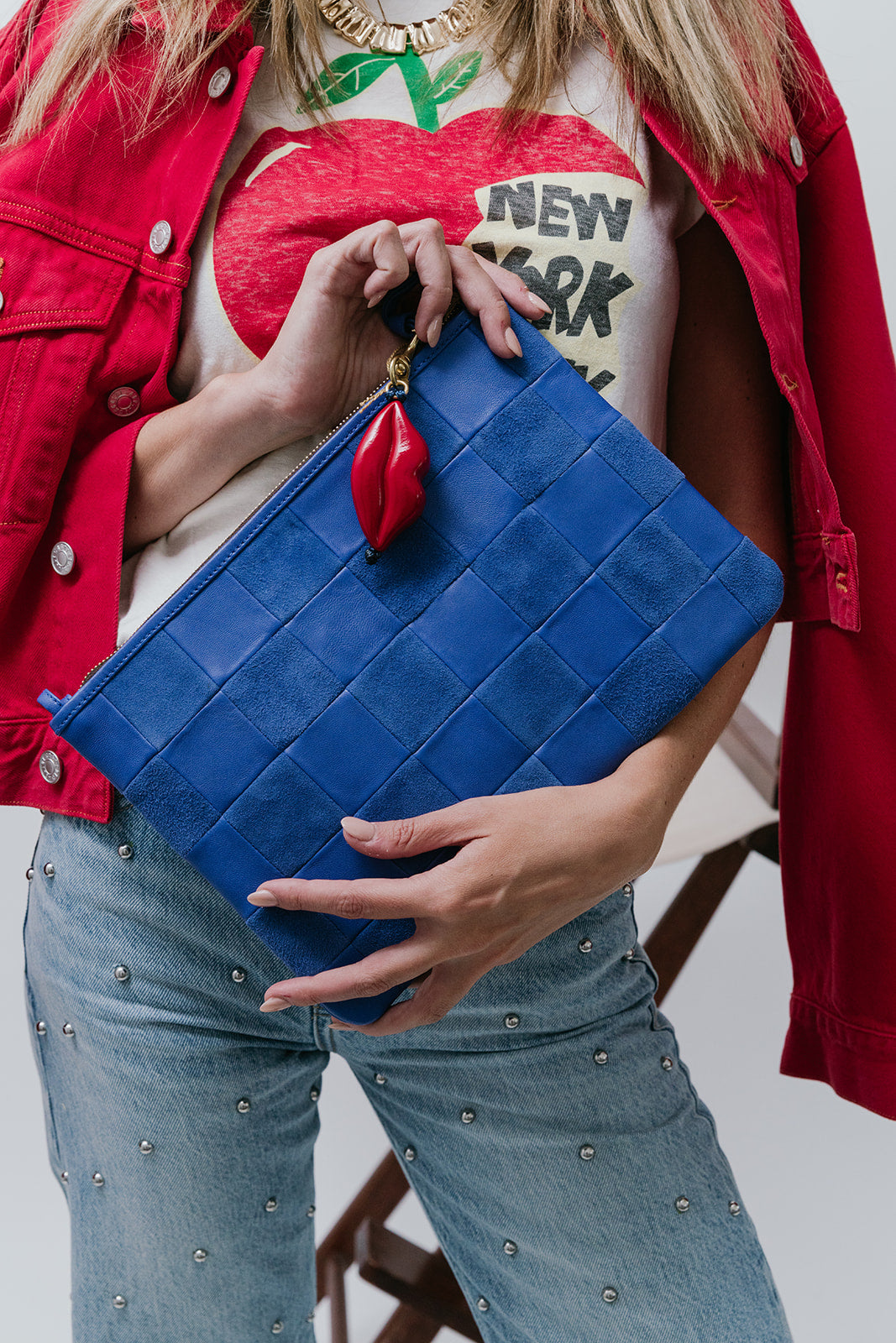 Person holding a blue clutch with a red detail, wearing a red jacket and jeans.