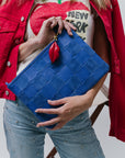 Person holding a blue clutch with a red detail, wearing a red jacket and jeans.