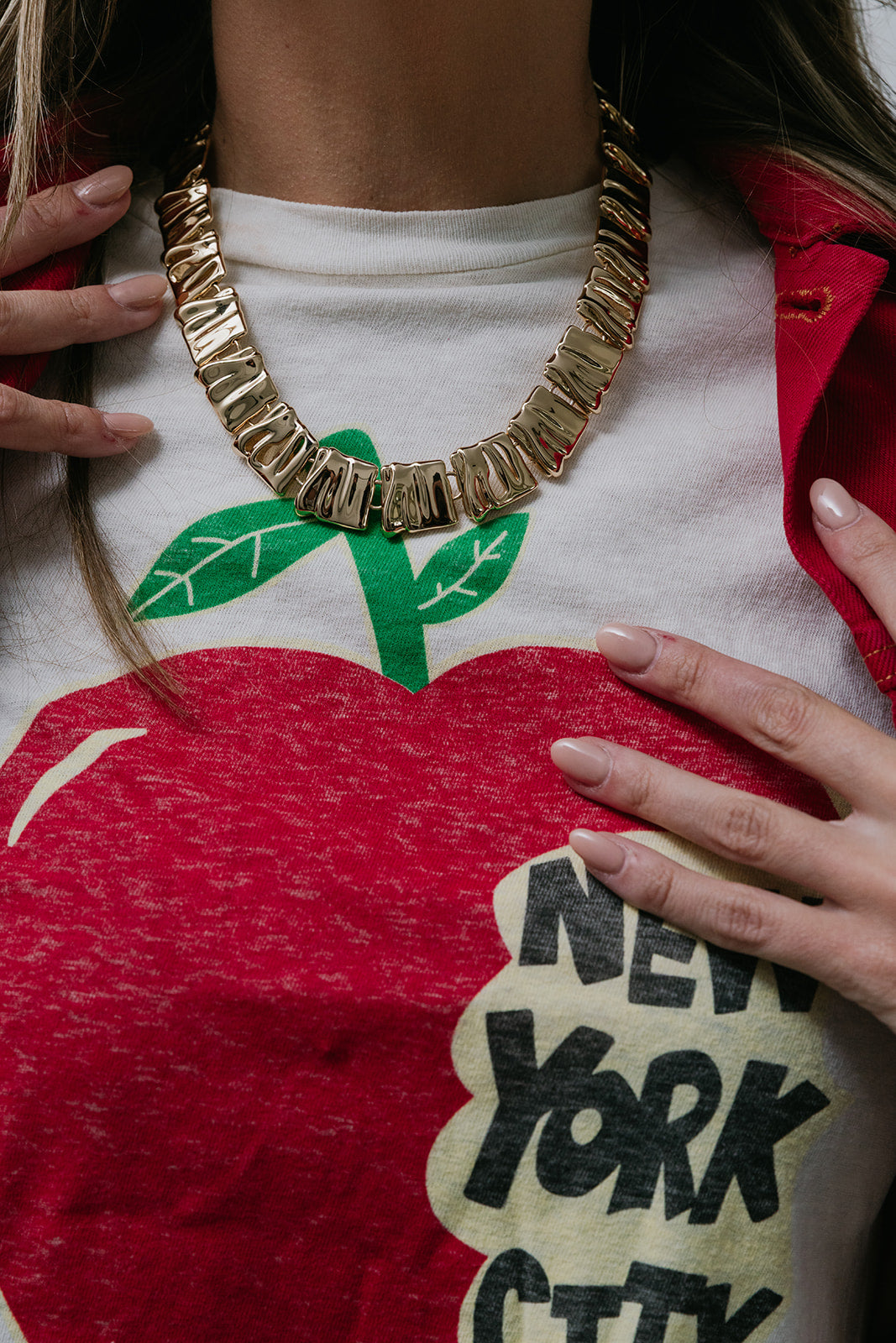 Person wearing a white shirt with a red apple graphic and 'New York City' text, accessorized with a gold necklace.