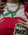 Person wearing a white shirt with a red apple graphic and 'New York City' text, accessorized with a gold necklace.