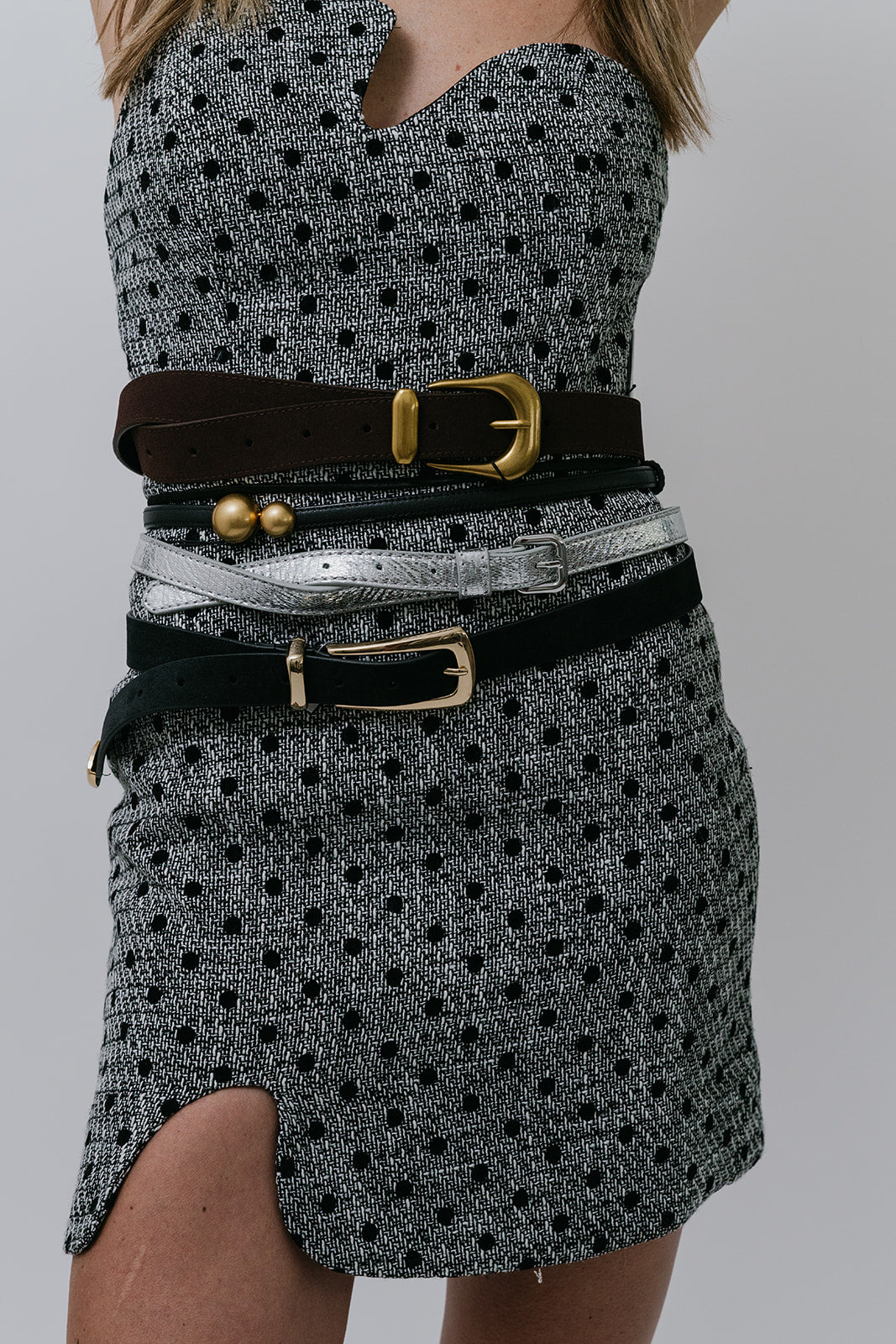 Person wearing a patterned dress with multiple belts and buckles on a gray background, close up 