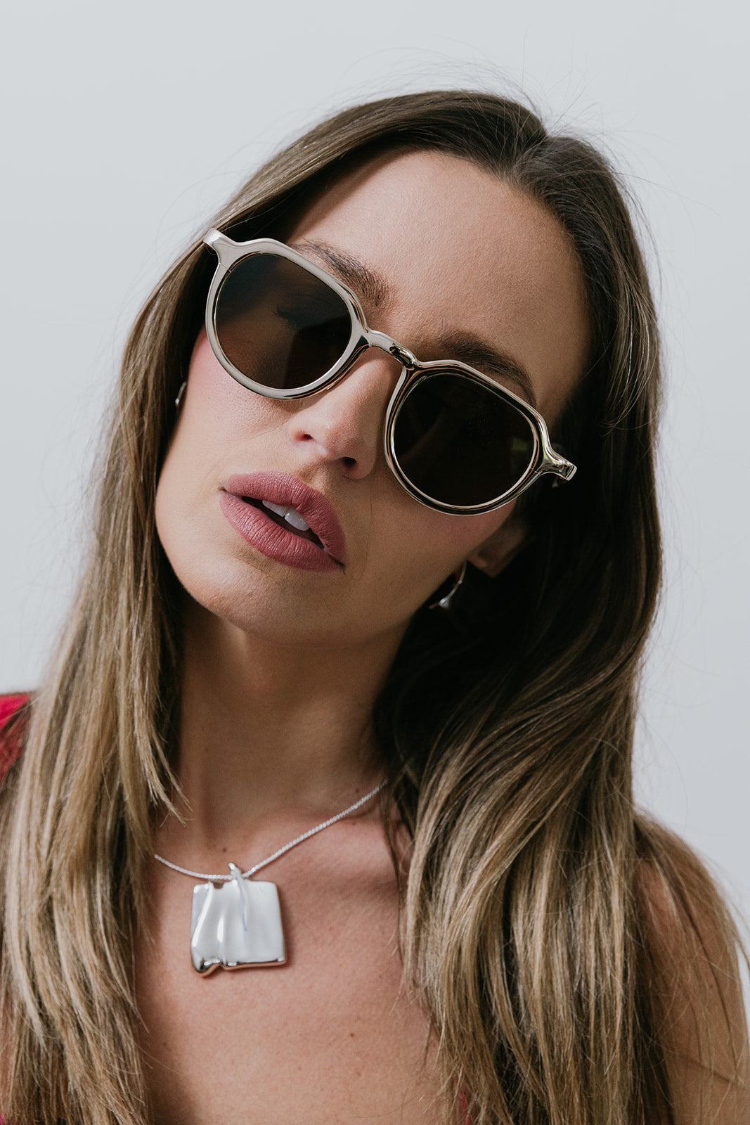 Woman wearing round sunglasses and silver necklace with a neutral background