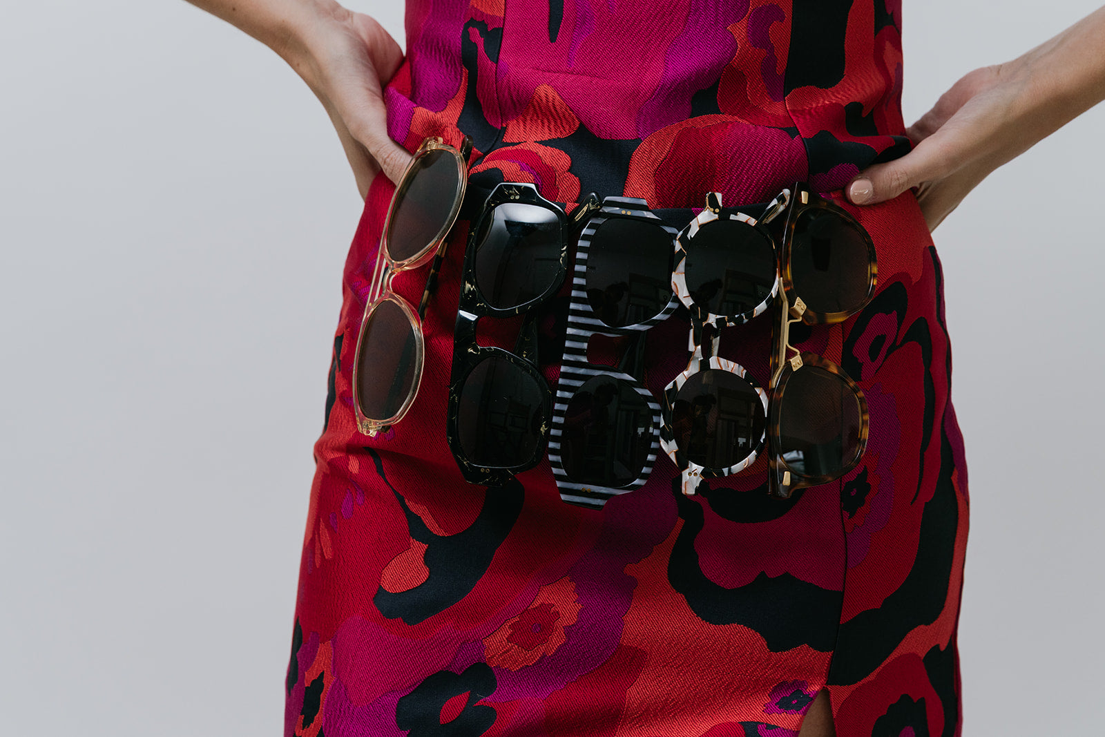 Person holding a collection of sunglasses against a plain background