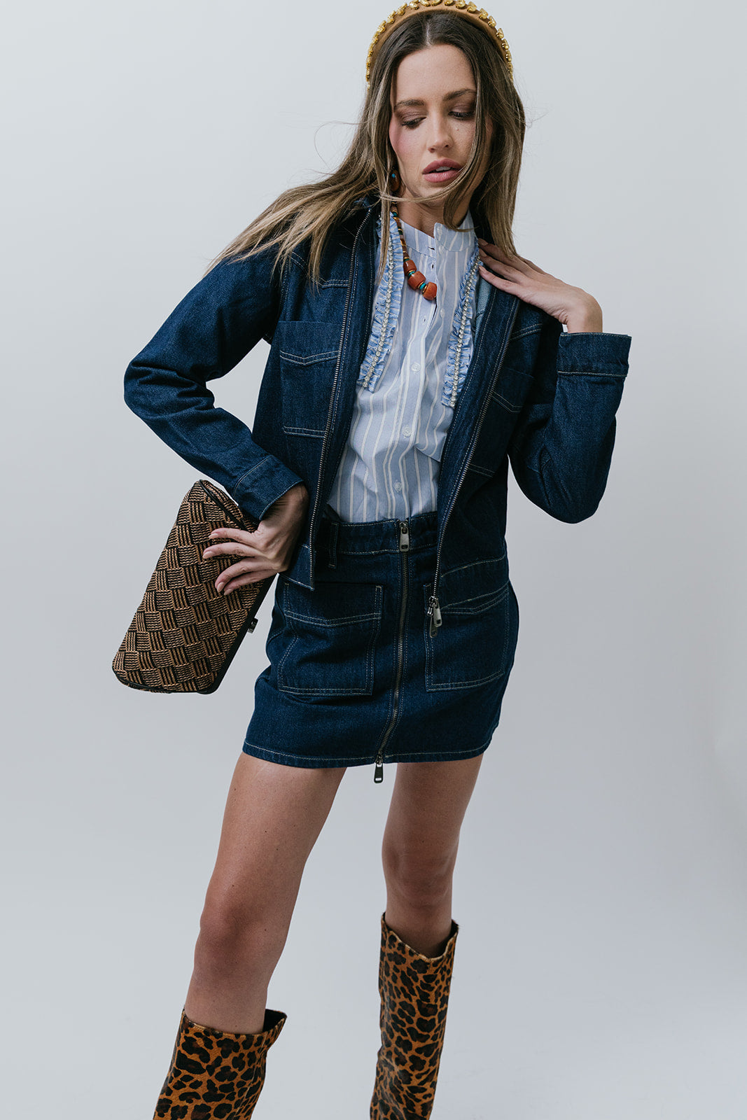 Woman wearing a denim outfit with leopard print boots and clutch against a plain background