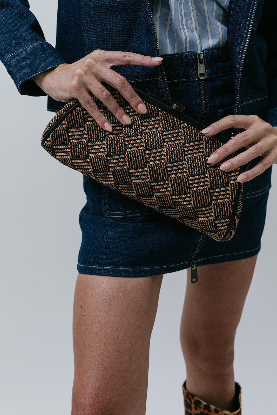 Person holding a woven clutch bag with a plain background