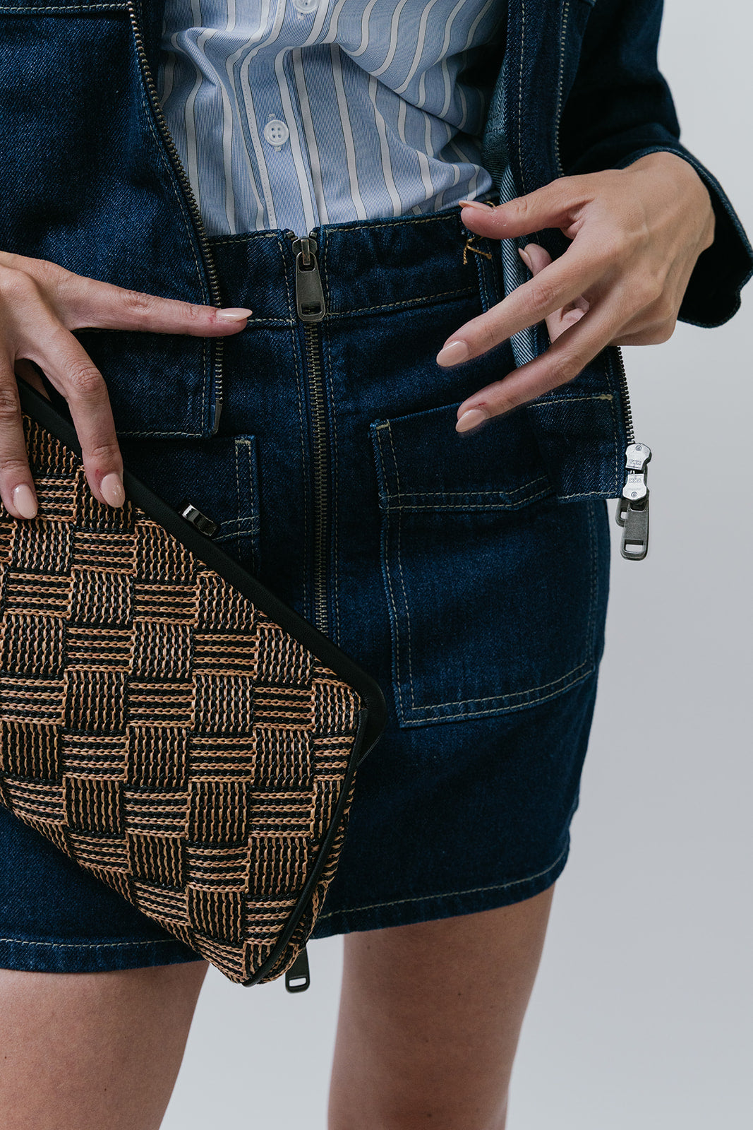 Person wearing a denim skirt with a patterned bag and striped shirt on a plain background