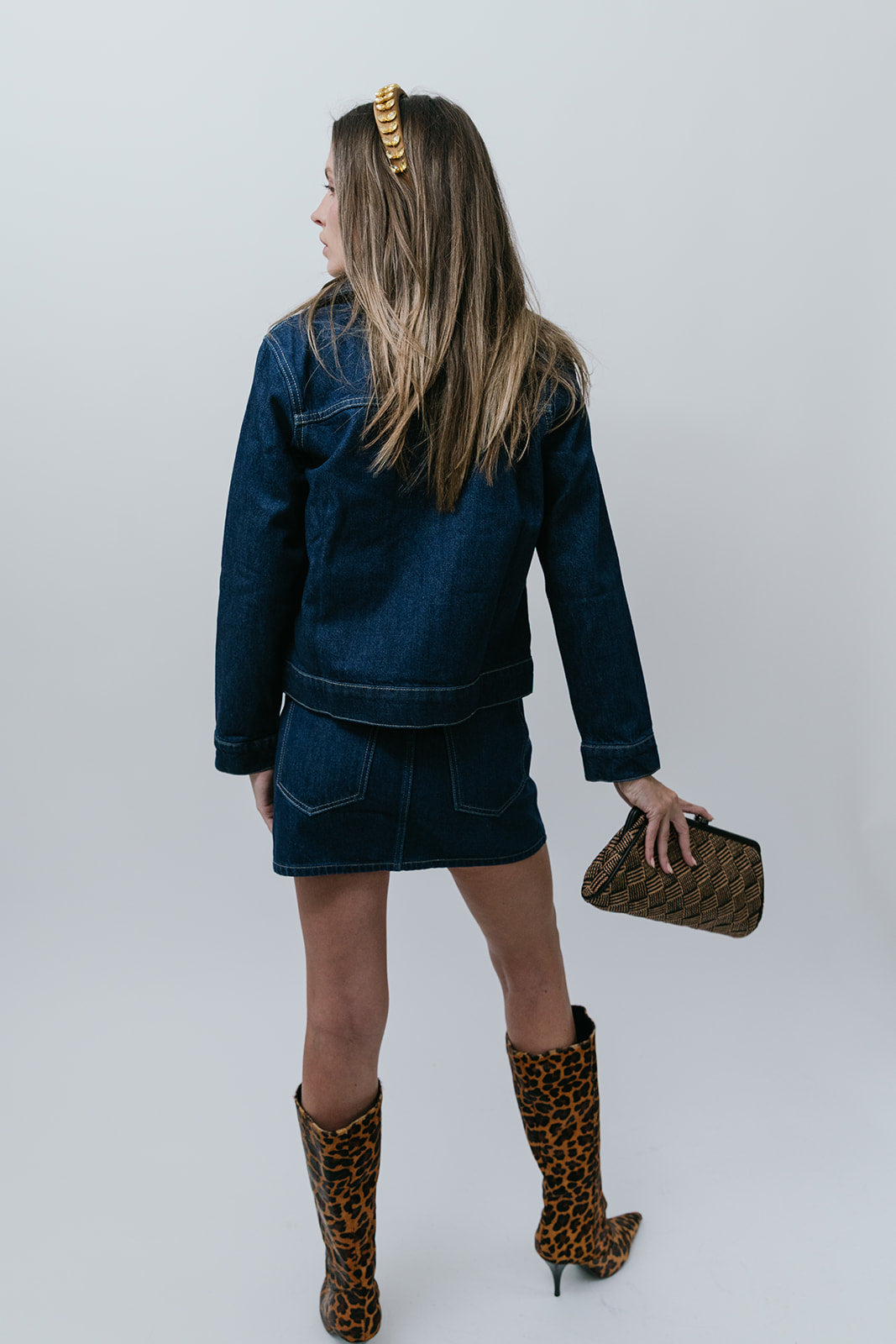 Person wearing a denim outfit with leopard print boots and clutch on a white background, back