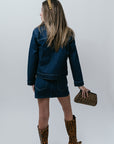 Person wearing a denim outfit with leopard print boots and clutch on a white background, back
