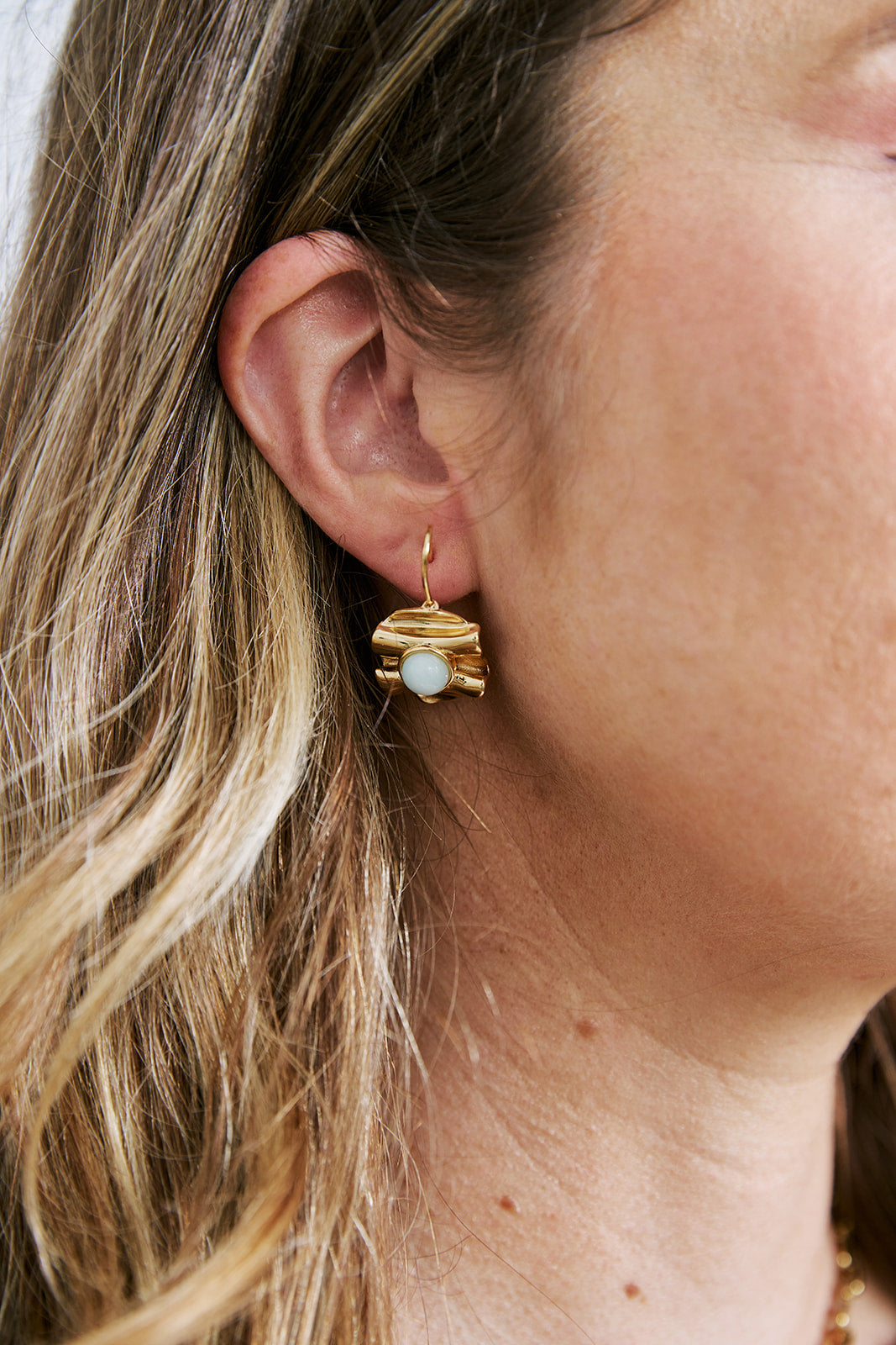 Close-up of a person wearing gold earrings with a central gemstone.