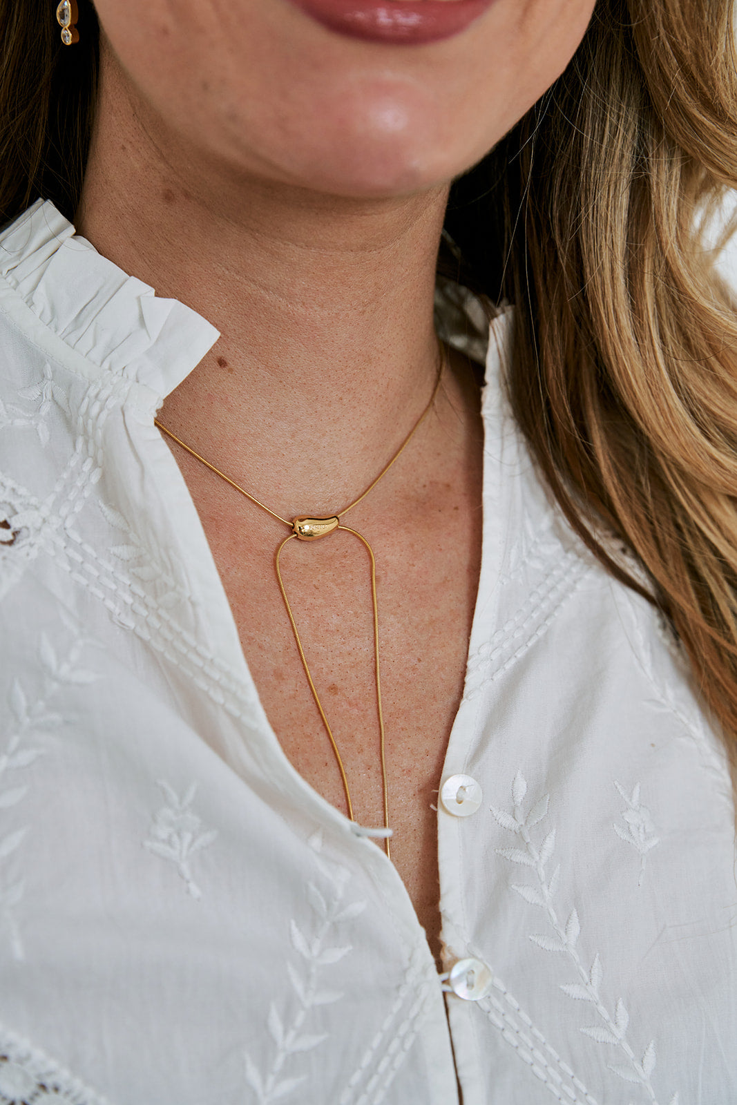 Close-up of a person wearing a gold necklace against a white blouse.