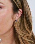 Close-up of a person wearing a gold fish earring with a blue gemstone.