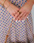 Close-up of hands with gold bracelets holding small stones, wearing a patterned dress.