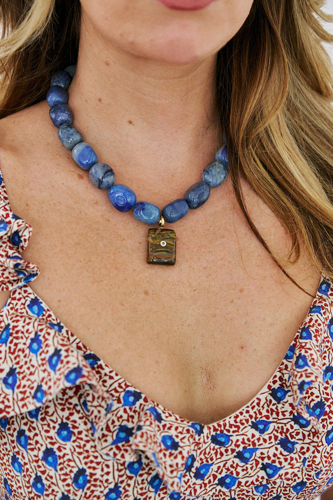 Close-up of a person wearing a blue beaded necklace with a pendant.