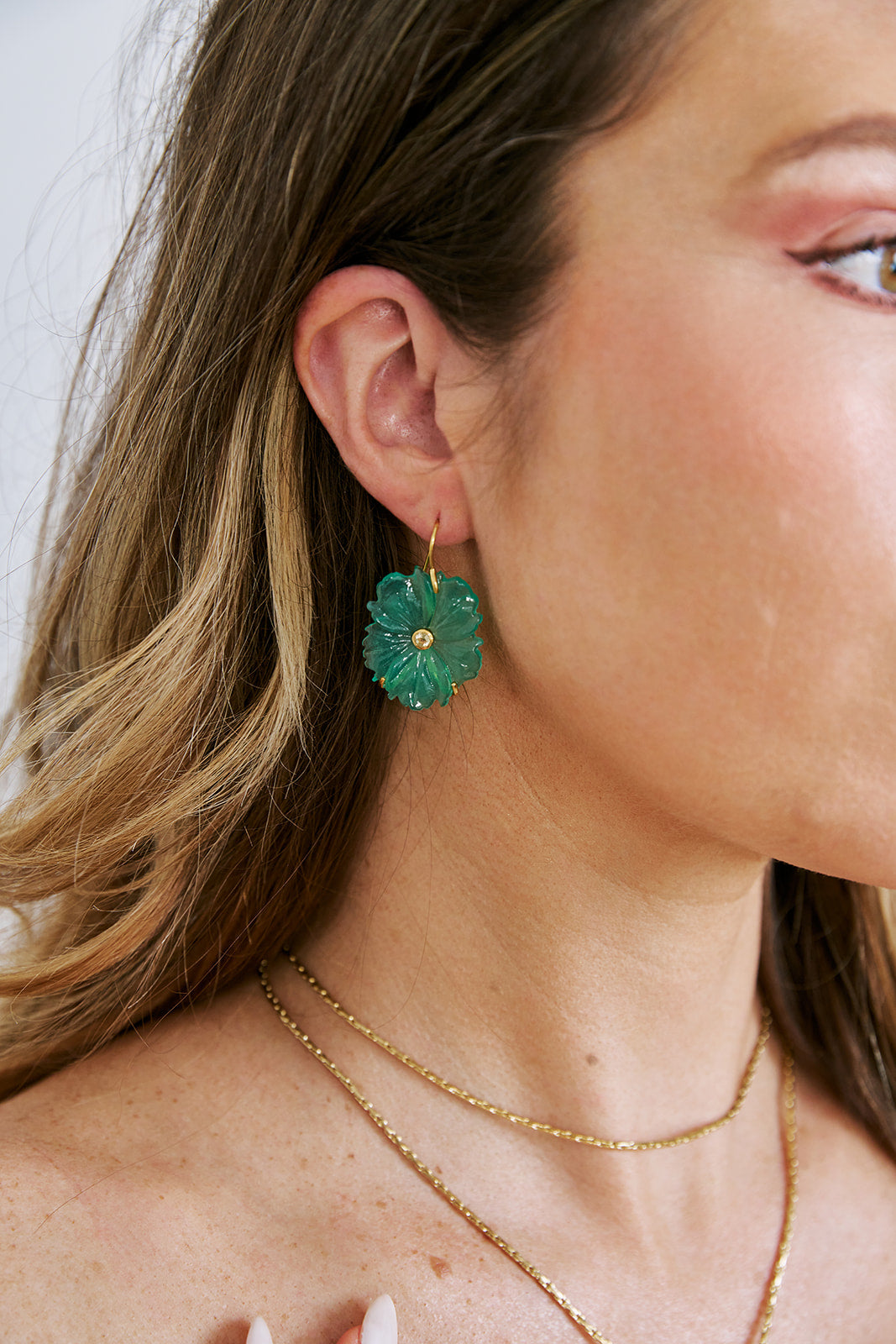 Close-up of a person wearing green floral earrings and a gold necklace.