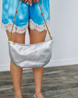 Person wearing blue shorts with lace trim holding a silver handbag on a wooden floor.