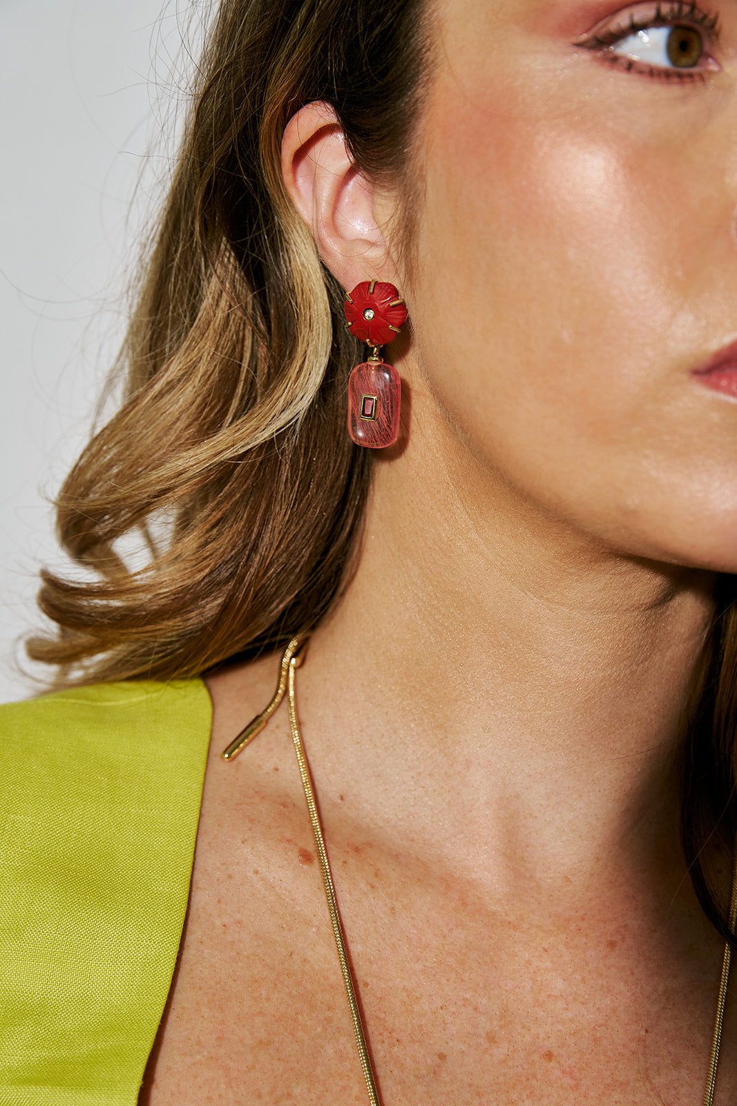 Close-up of a woman wearing red floral earrings with a gold necklace.