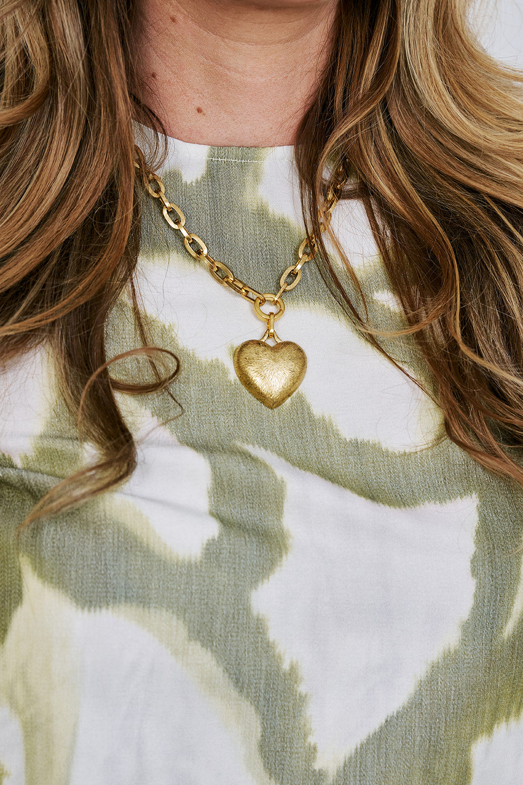 Close-up of a person wearing a gold necklace with a heart pendant