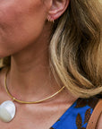 Close-up of a woman wearing a delicate gold necklace with a large white oval pendant and Quinn Hoop Earrings, paired with a blue patterned top.