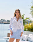 Woman in a white and blue striped shirt and skirt standing by a pool with a scenic background.