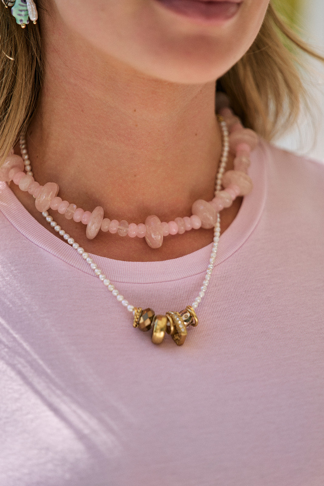 Close-up of a person wearing a necklace with pink beads and necklace with gold accents on a pink shirt.