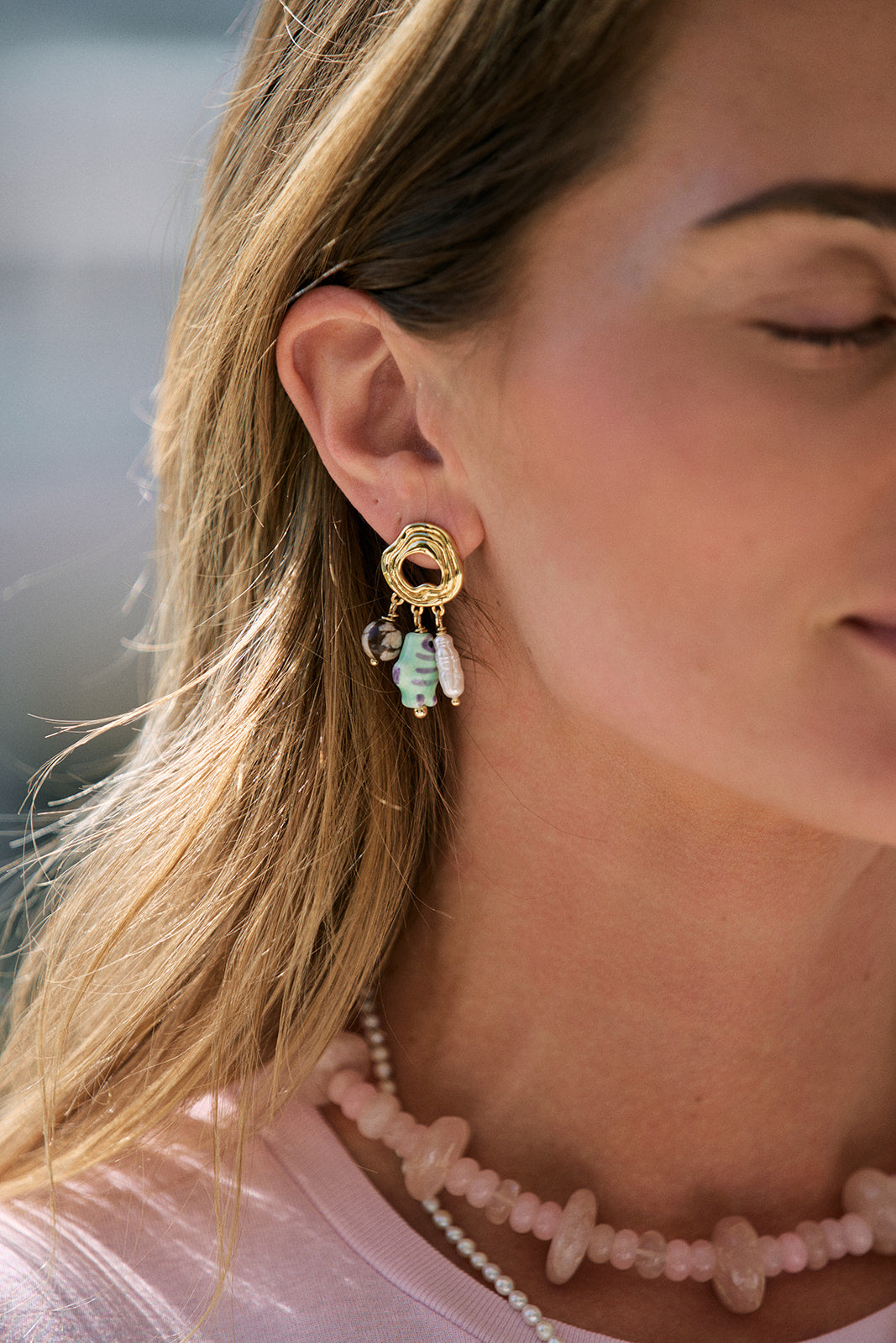 Close-up of a woman wearing gold earrings with green and clear beads, blurred background