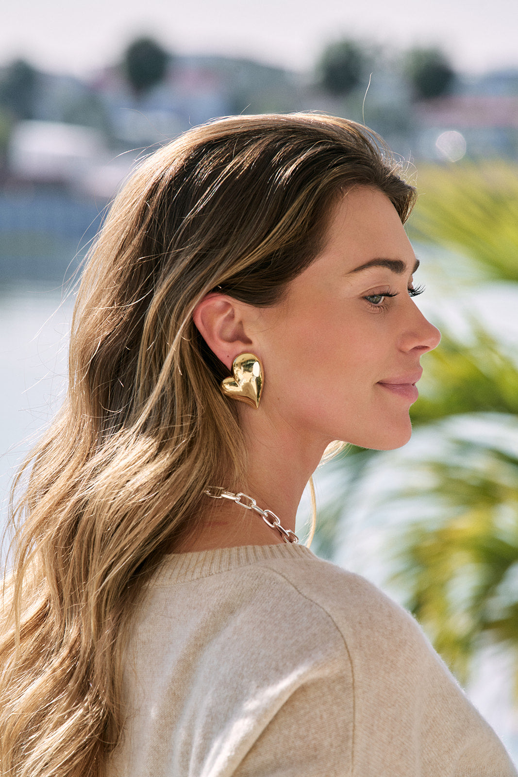 Woman wearing gold earrings with a blurred outdoor background