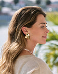 Woman wearing gold earrings with a blurred outdoor background