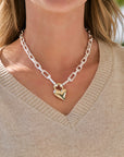 Close-up of a person wearing a gold heart-shaped pendant on a chain necklace.