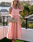 Woman in a pink dress standing on a balcony with a waterfront view.