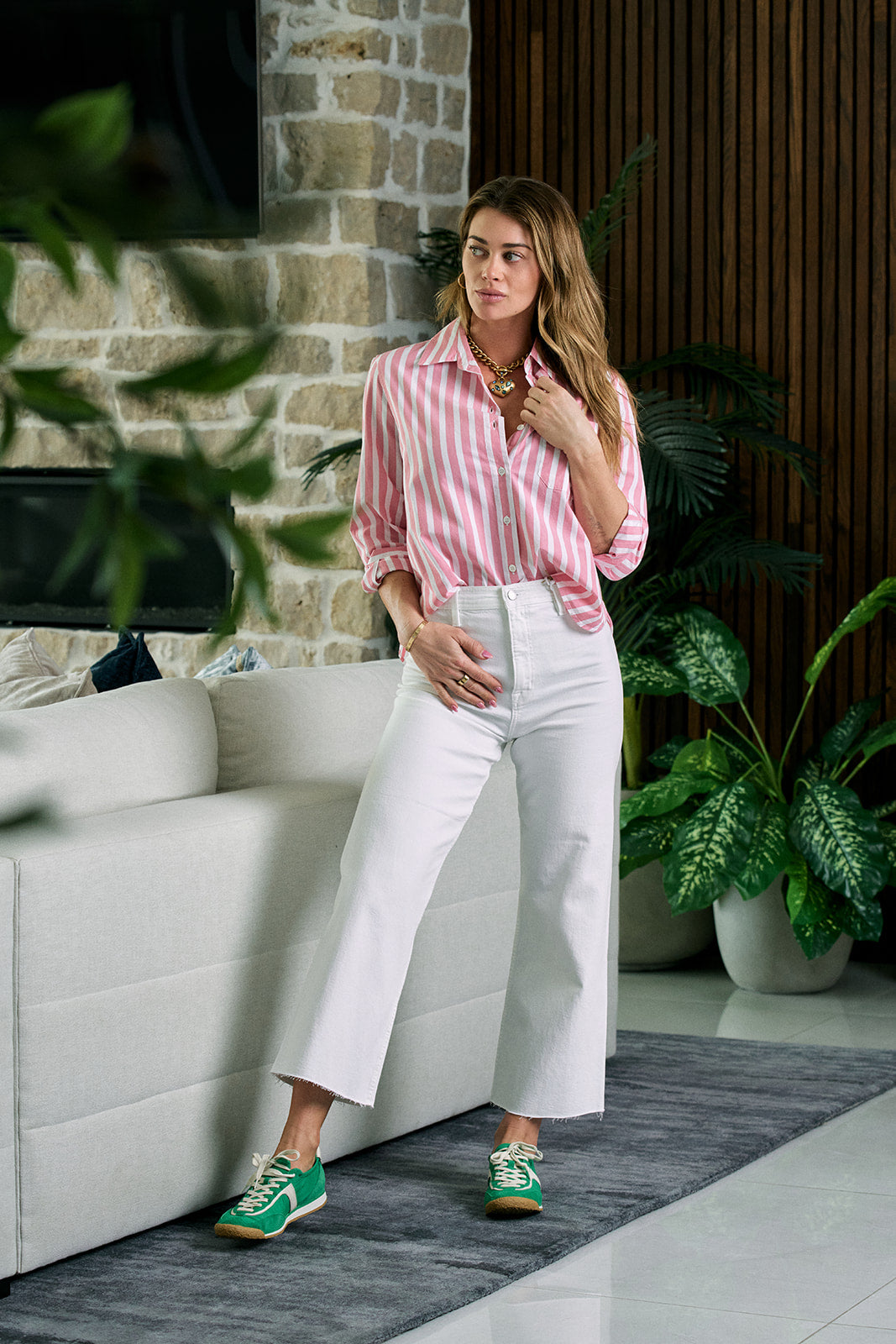 Woman in a pink striped shirt and white pants standing in a modern living room.
