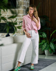 Woman in a pink striped shirt and white pants standing in a modern living room.