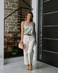 Woman wearing Memphis High Rise Pant and seaglass top standing in a modern interior setting with stone wall and staircase.