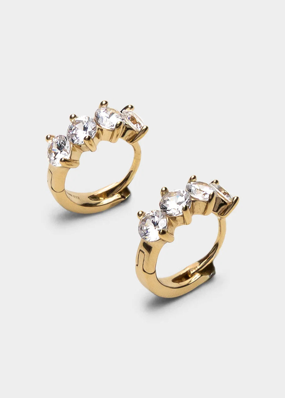 A pair of gold huggie hoop earrings with a curved top set with three clear marquise-cut gemstones, shown on a light gray background.