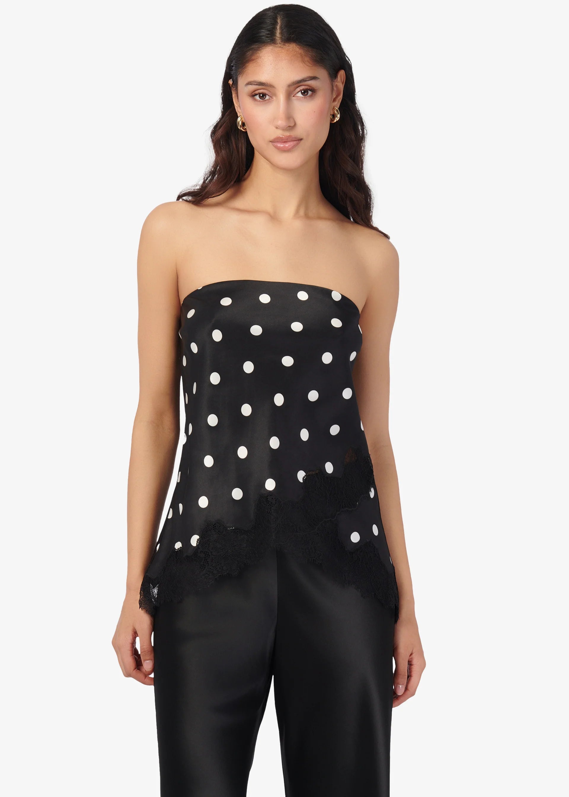 Woman wearing a black strapless top with white polka dots and black pants on a white background