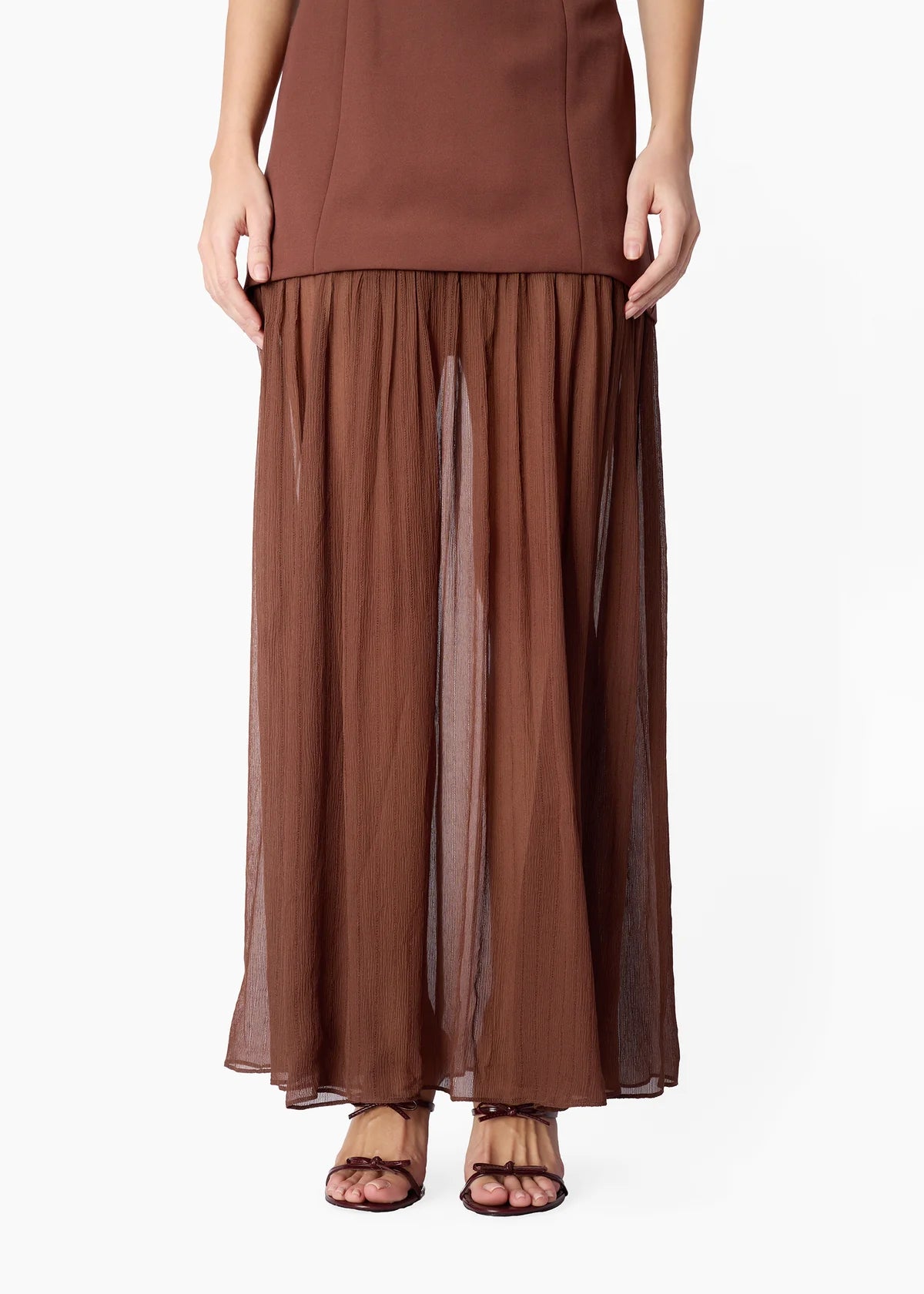 model wearing a brown dress on a white background, zoomed in on the bottom half sheer portion of the dress