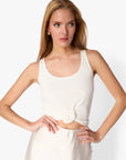 Woman wearing a white sleeveless top with a knot detail on a plain background
