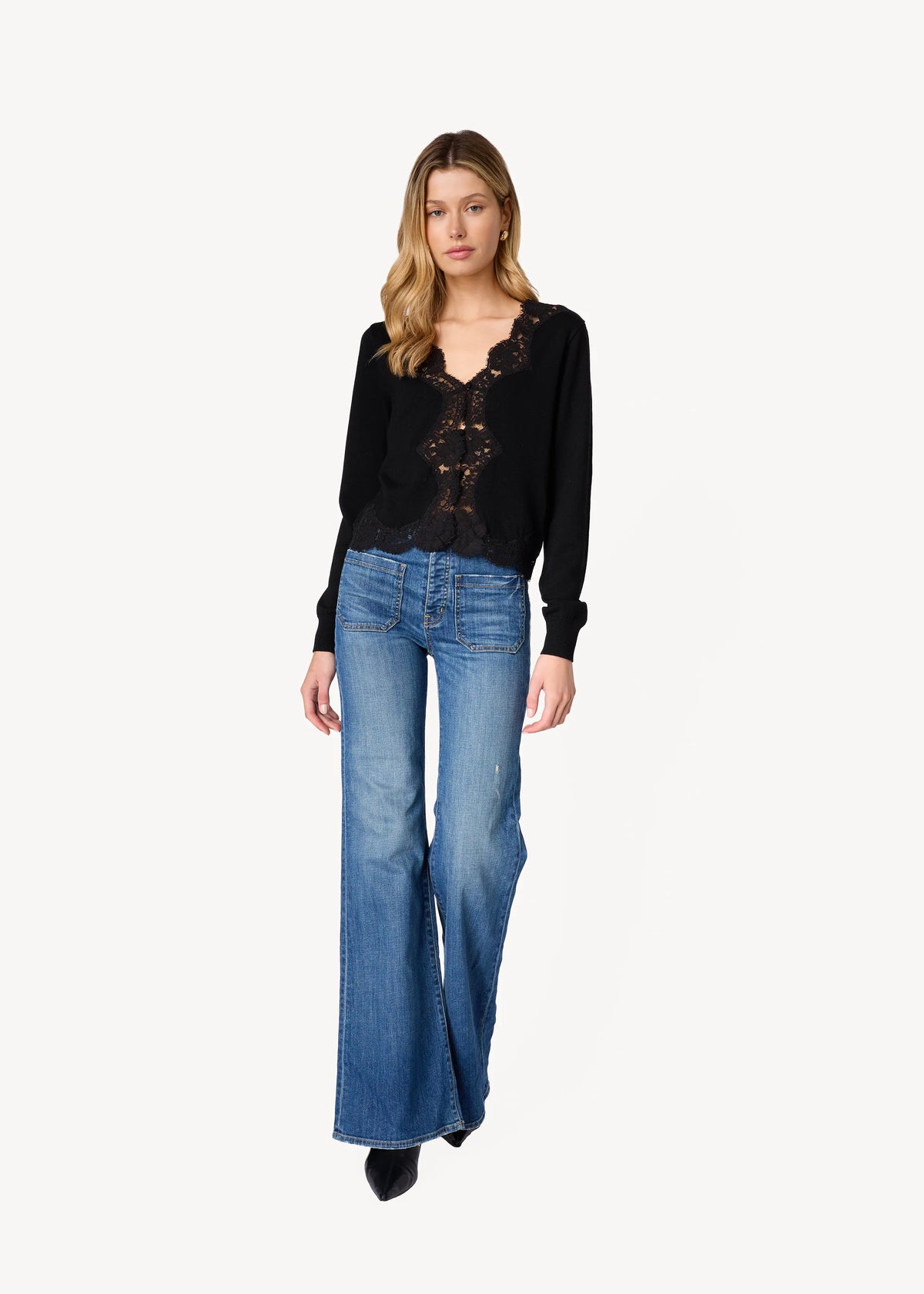 a model wearing a black cardigan with lace trim and blue jeans on a white background