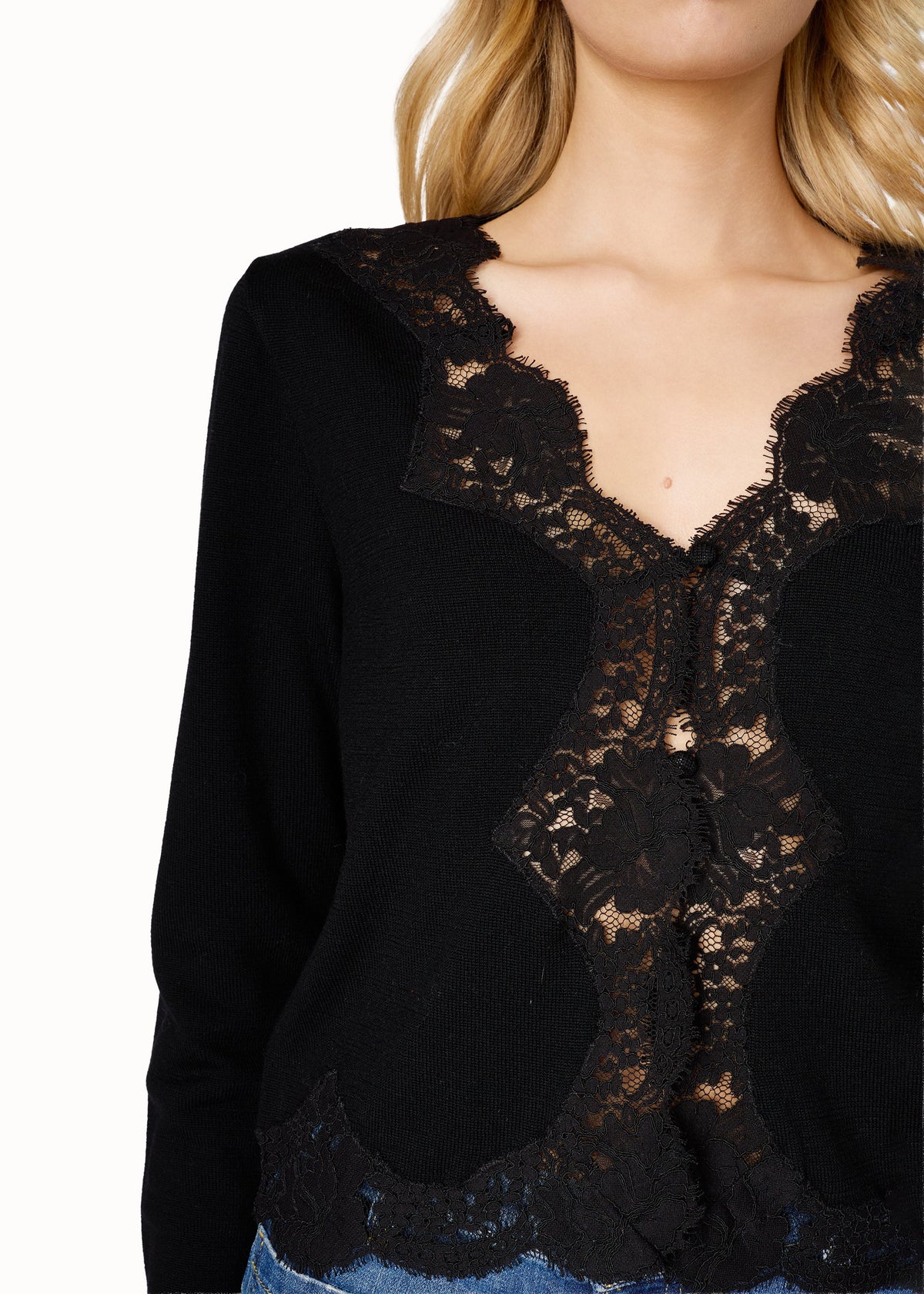 detail close up of a model wearing a black cardigan with lace trim and blue jeans on a white background