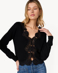 a model wearing a black cardigan with lace trim and blue jeans on a white background