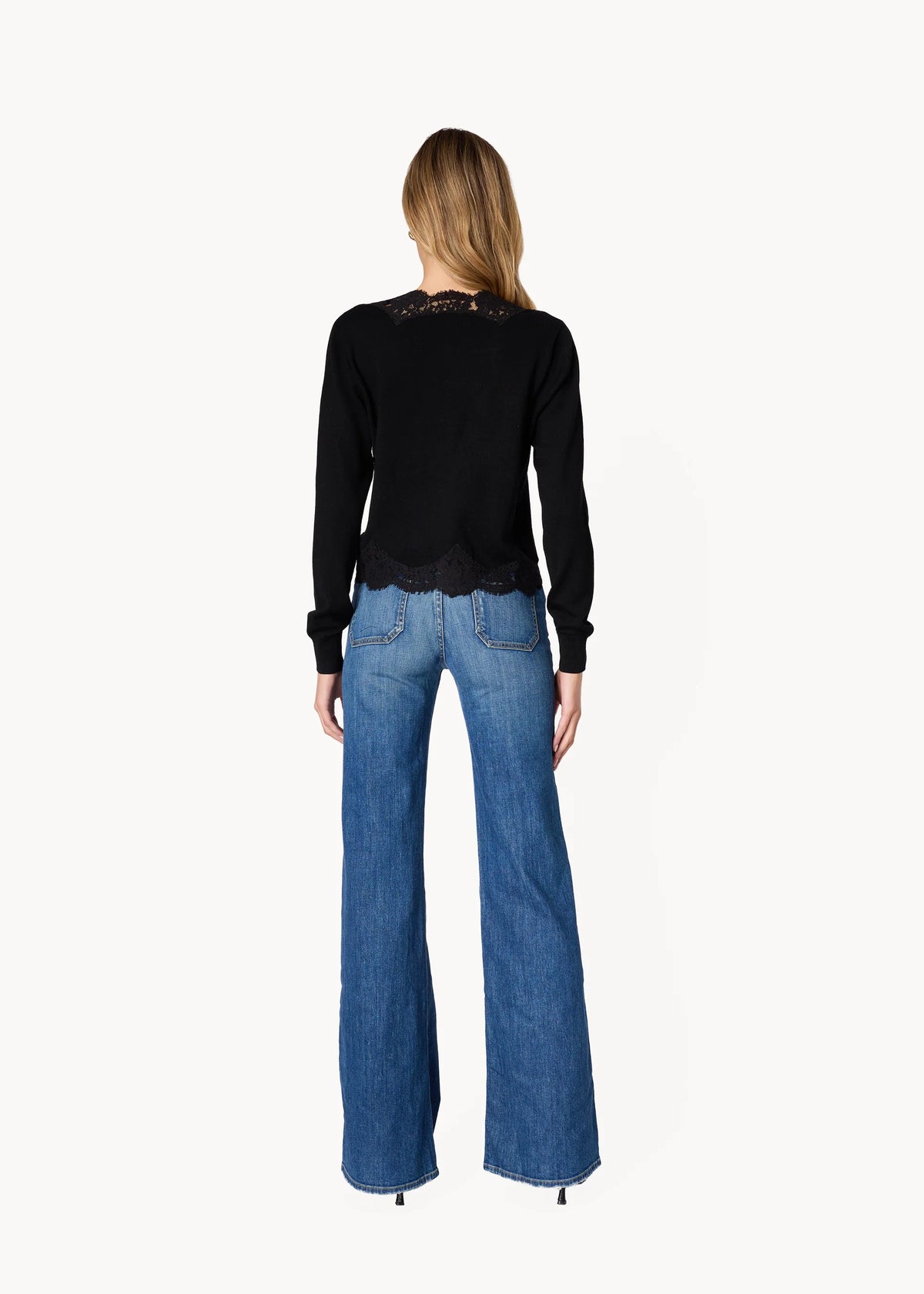 a model wearing a black cardigan with lace trim and blue jeans on a white background, back view