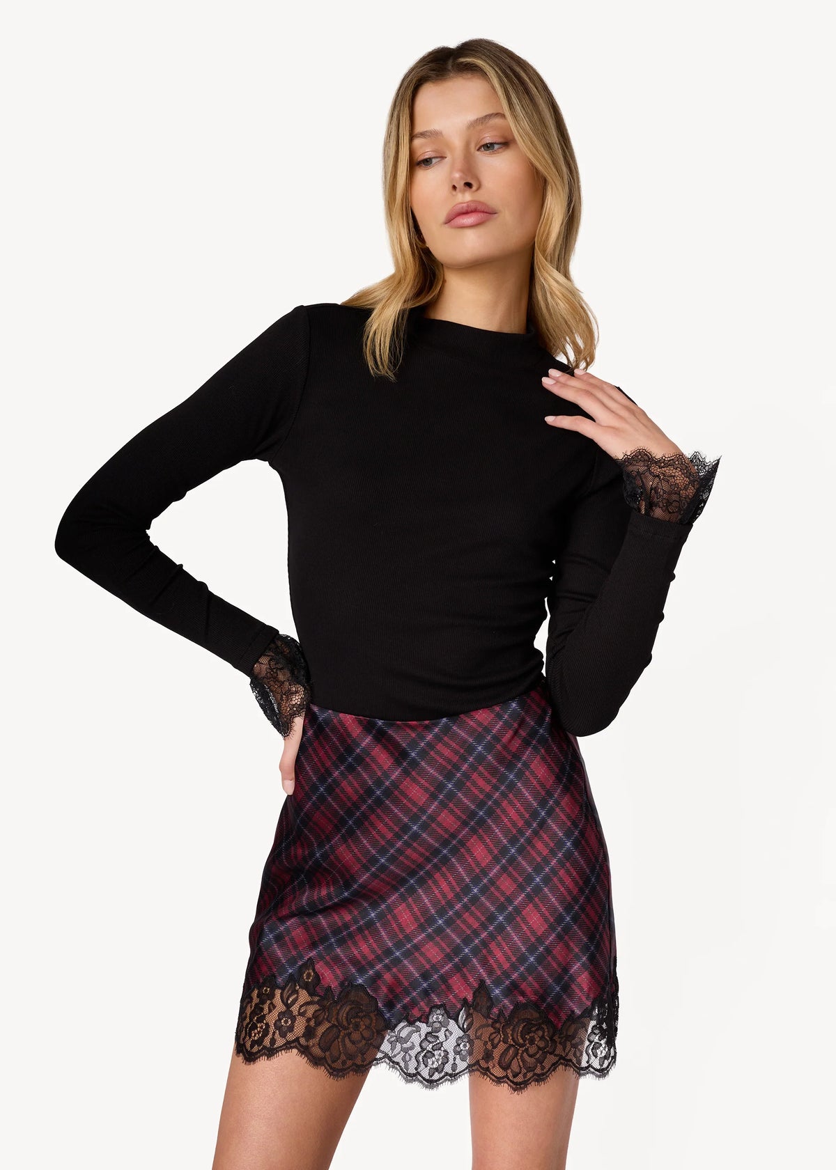 model wearing a long sleeve black top with lace at the wrist with a plaid mini skirt with lace trim on a white background