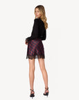 model wearing a long sleeve black top with lace at the wrist with a plaid mini skirt with lace trim on a white background, back view