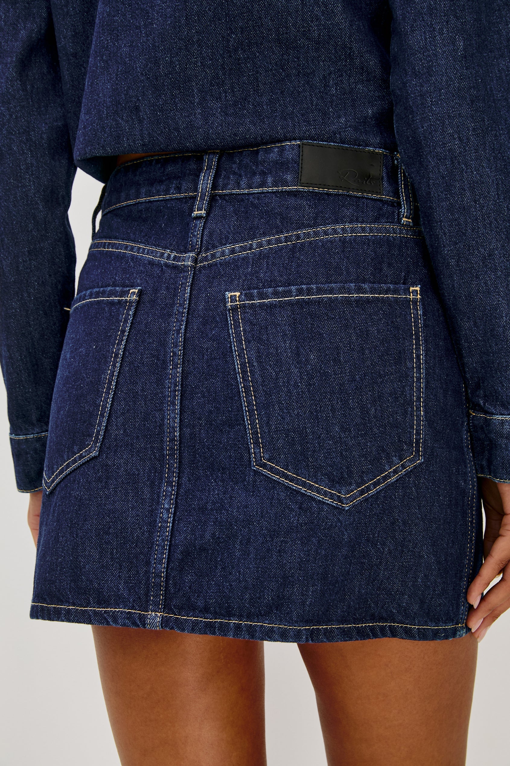 Denim skirt worn by a person on a plain background, back close up