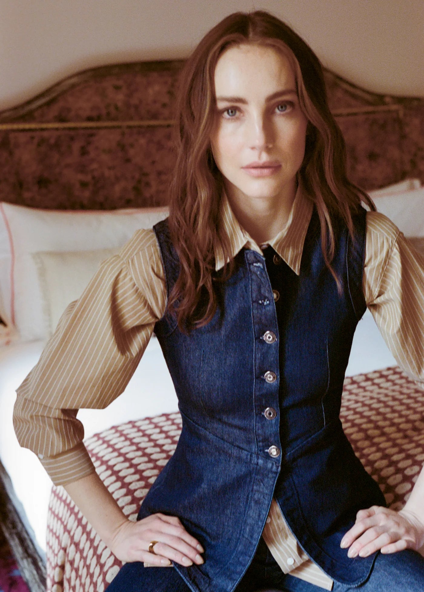 Woman wearing a blue vest over a beige shirt in a bedroom setting