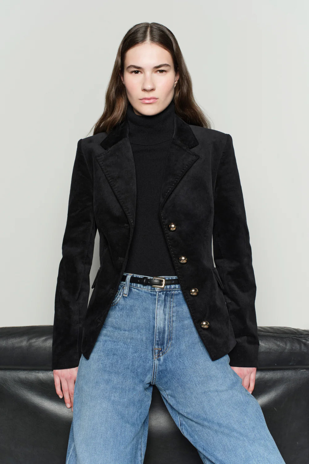 Person wearing a black blazer and blue jeans on a plain background