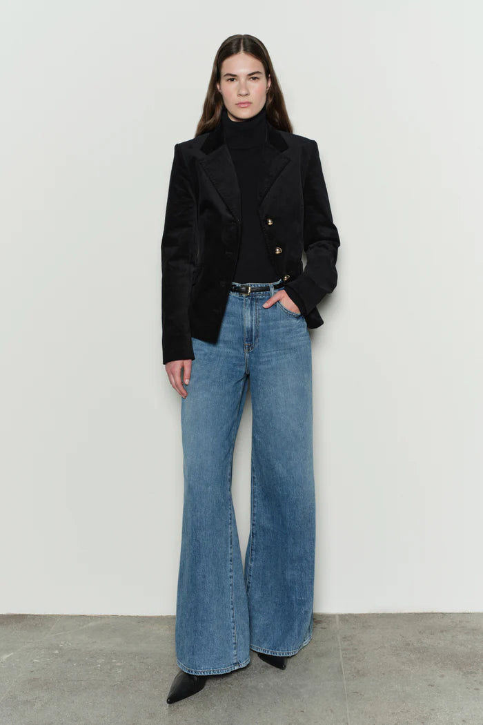 Person wearing a black coat and blue jeans against a white background