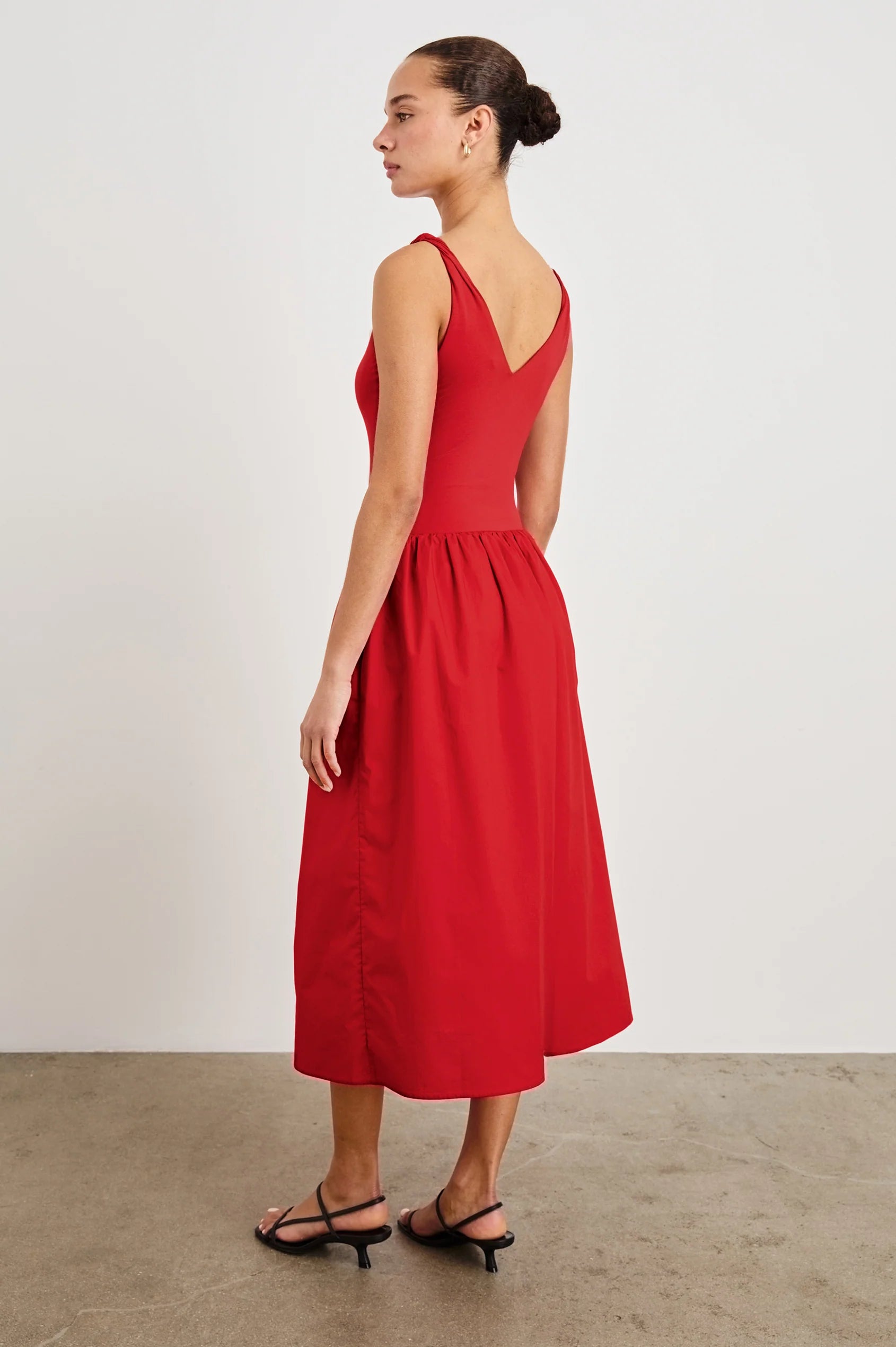 Woman wearing a red dress with cut-out back on a plain background side back view